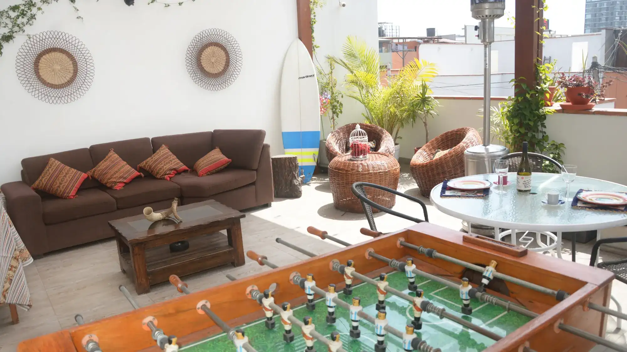 Sofá y mesa de la terraza compartida, con el futbolín y una tabla de surf al fondo